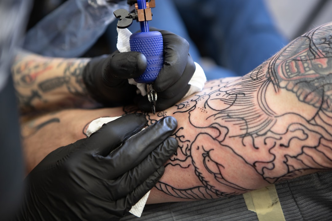 Gloved hands tattooing an arm.