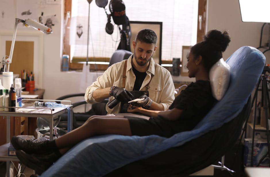 Woman getting a tattoo and a tattoo artist in white jacket.
