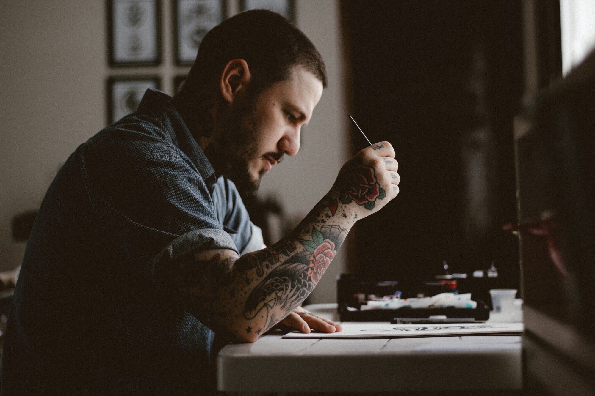 Man with tattoo on arm - a tattoo artist reading a paper on a desk.