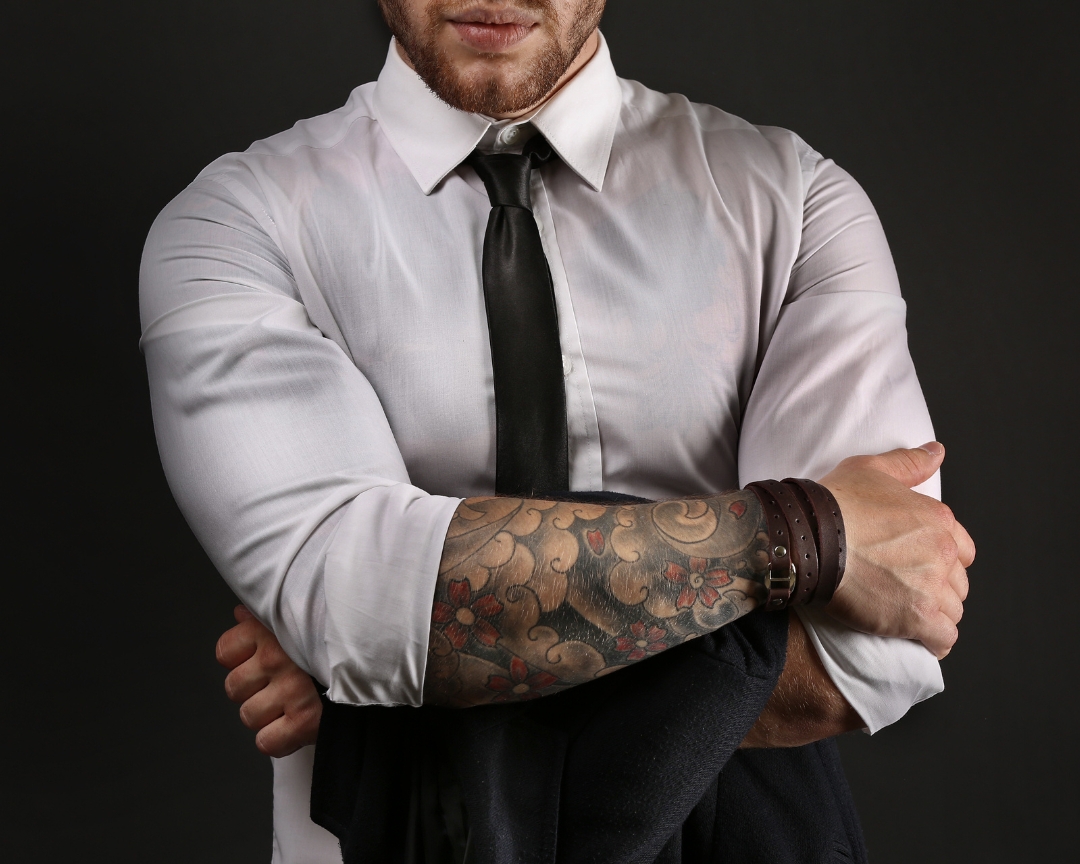 A man in white polo and tie with tattoo shown on one arm
