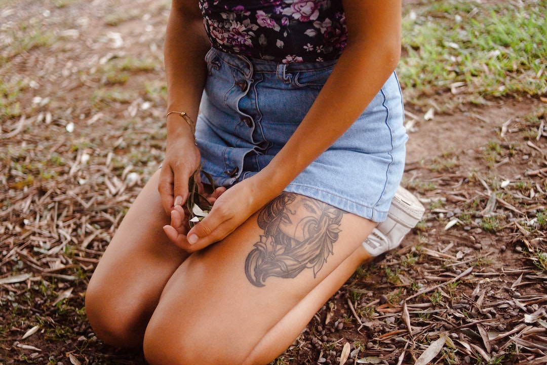 Woman kneeling on the ground on short pants showing tattoo on thigh.